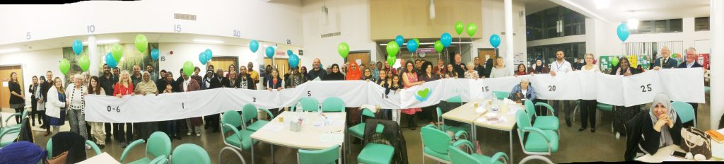 Photo of a lot of people holding up a long timeline at the DWB AGM, holding balloons