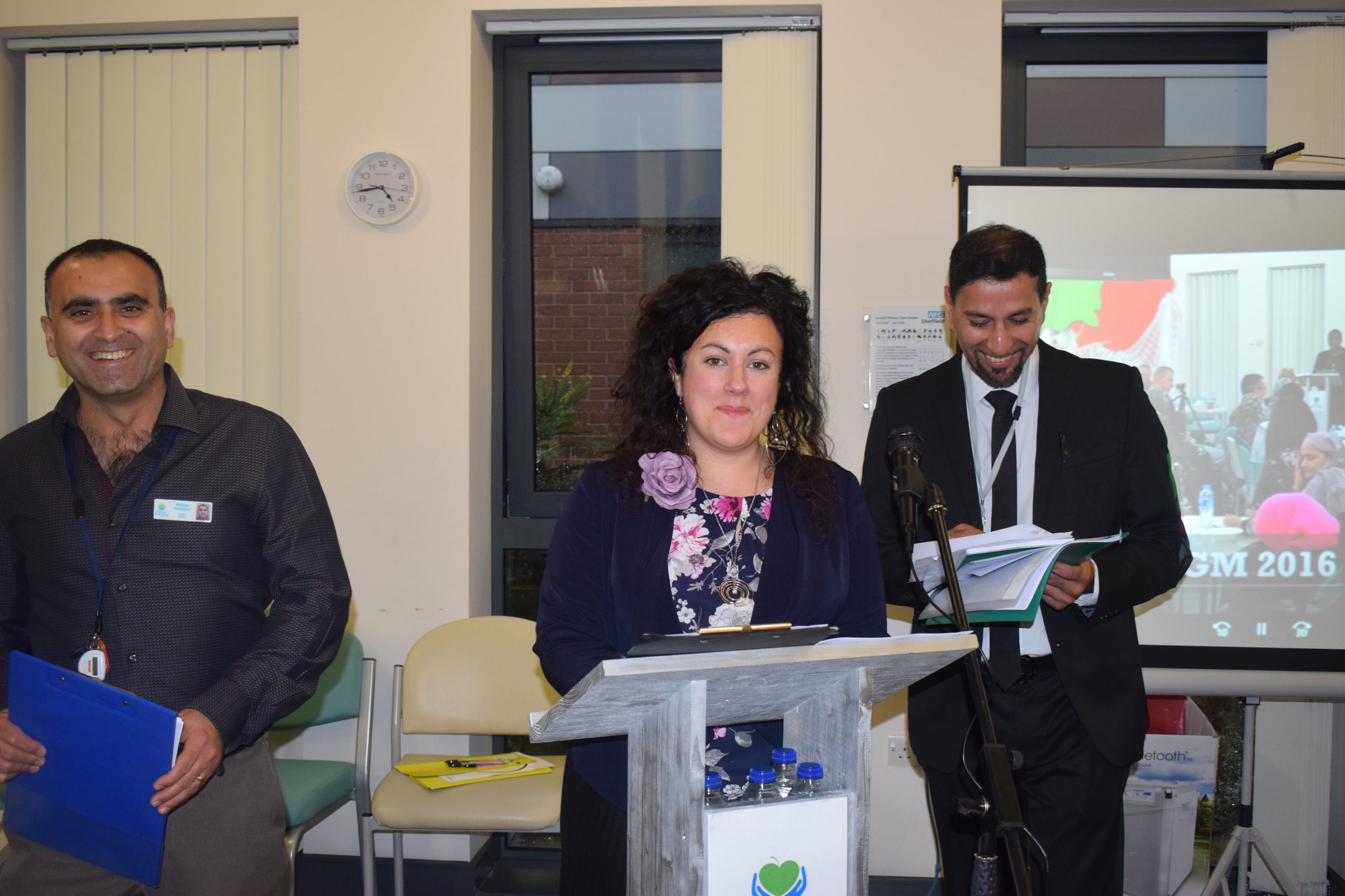 photo of Lucy Melleney, CEO of DWB, at a lectern with 2 smiling people behind her