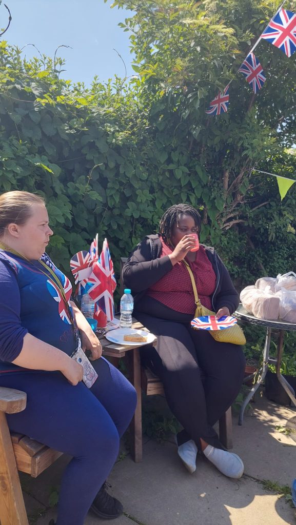 people sitting eating in sunshine beneath Union Jack bunting