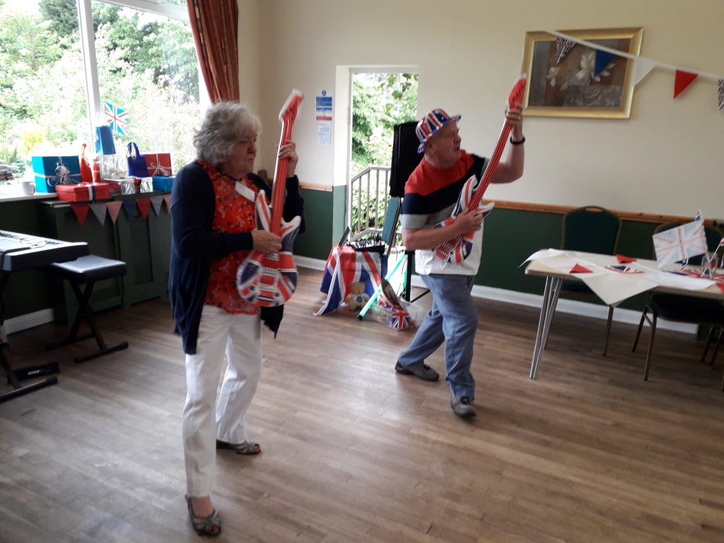 2 people playing inflatable Union Jack guitars in a church hall