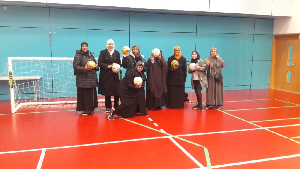 a group of women in headscarves, standing smiling together, holding footballs