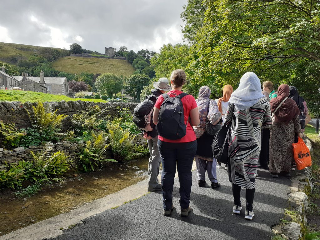 people standing with backs to the camera, looking up towards green hill with a castle tower on it.