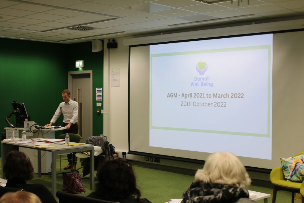 man standing at lectern next to large projector screen