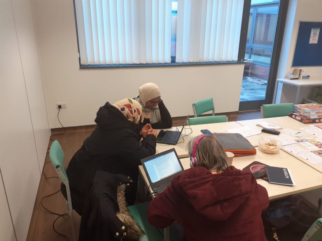 3 women seated around a table in a meeting room, looking at laptops together