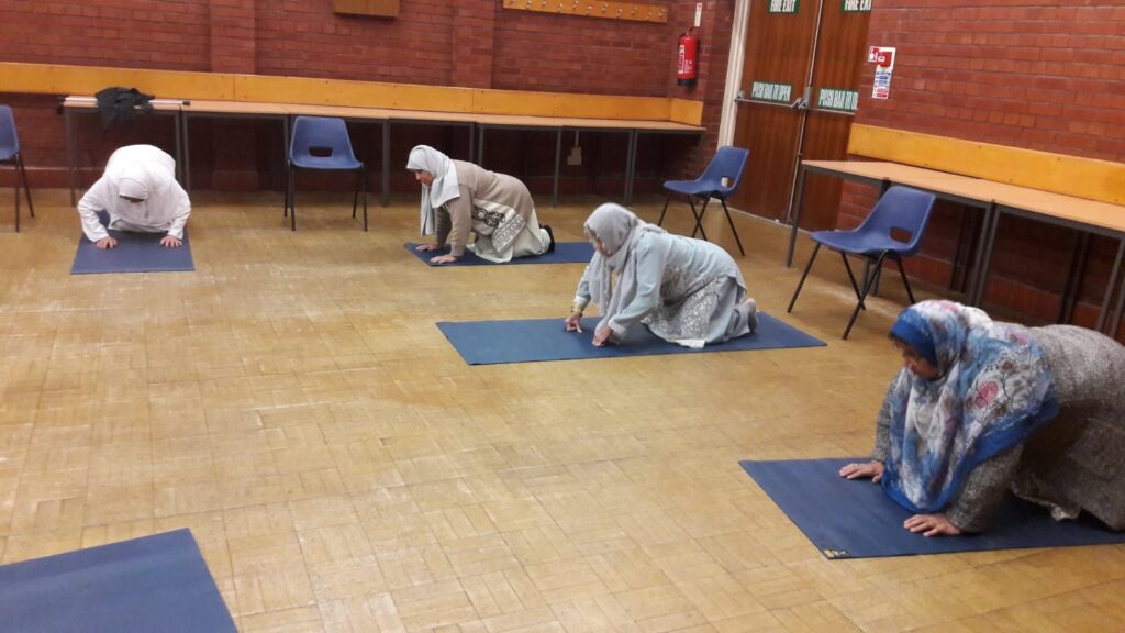 4 women kneeling on yoga mats in a community hall