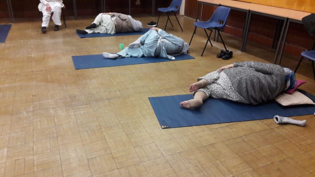 3 women lying on their sides on yoga mats in a community hall