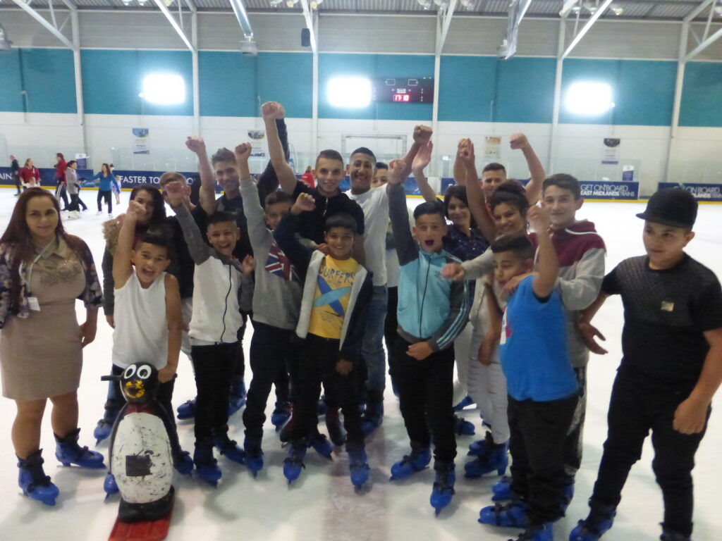 group of children standing on an ice rink, smiling with their arms in the air