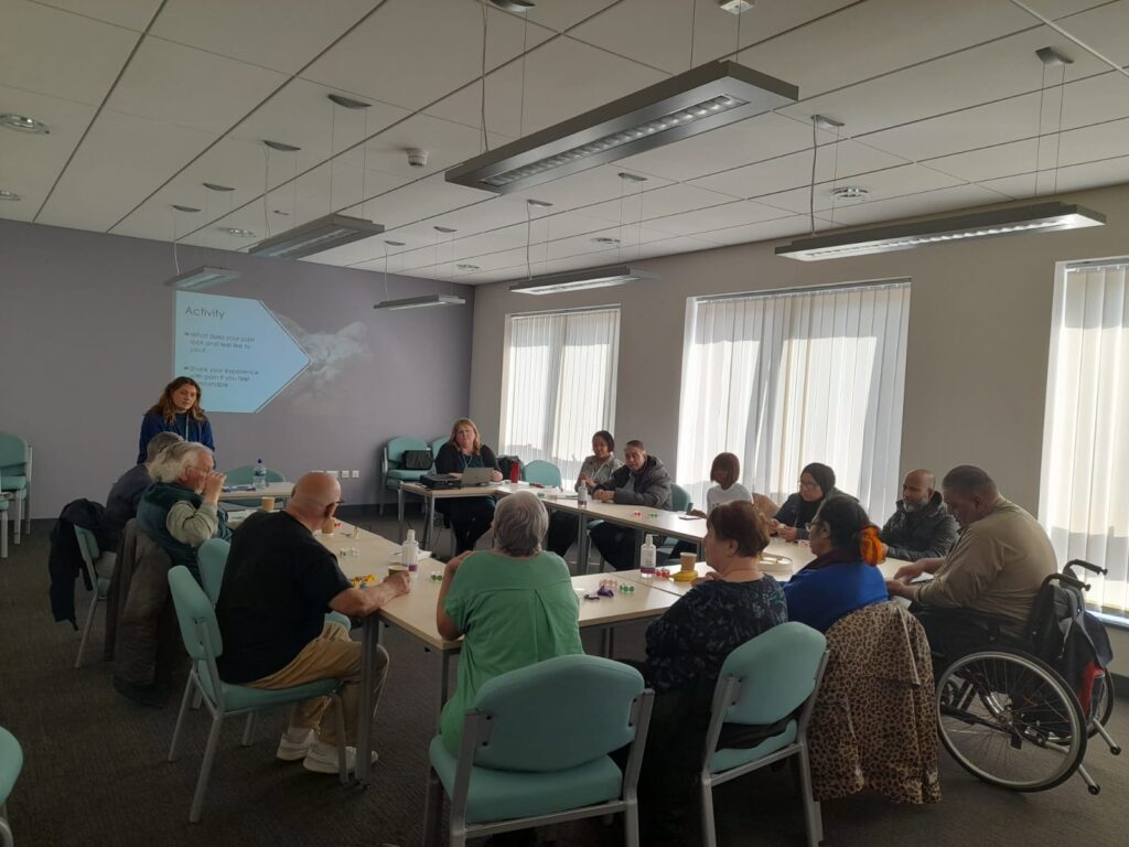 female student standing at the front of a meeting room, in front of a group of people seated around a table