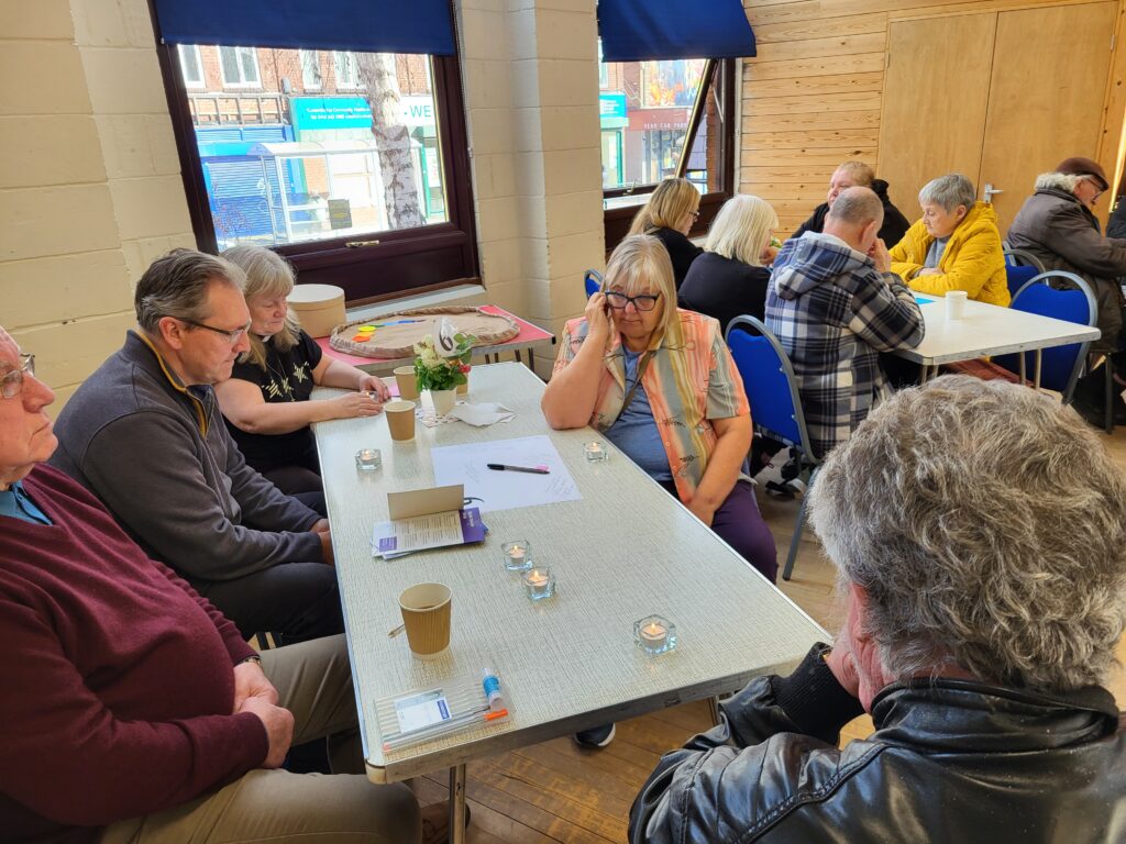 people seated around tables in a church hall with lit candles on the tables