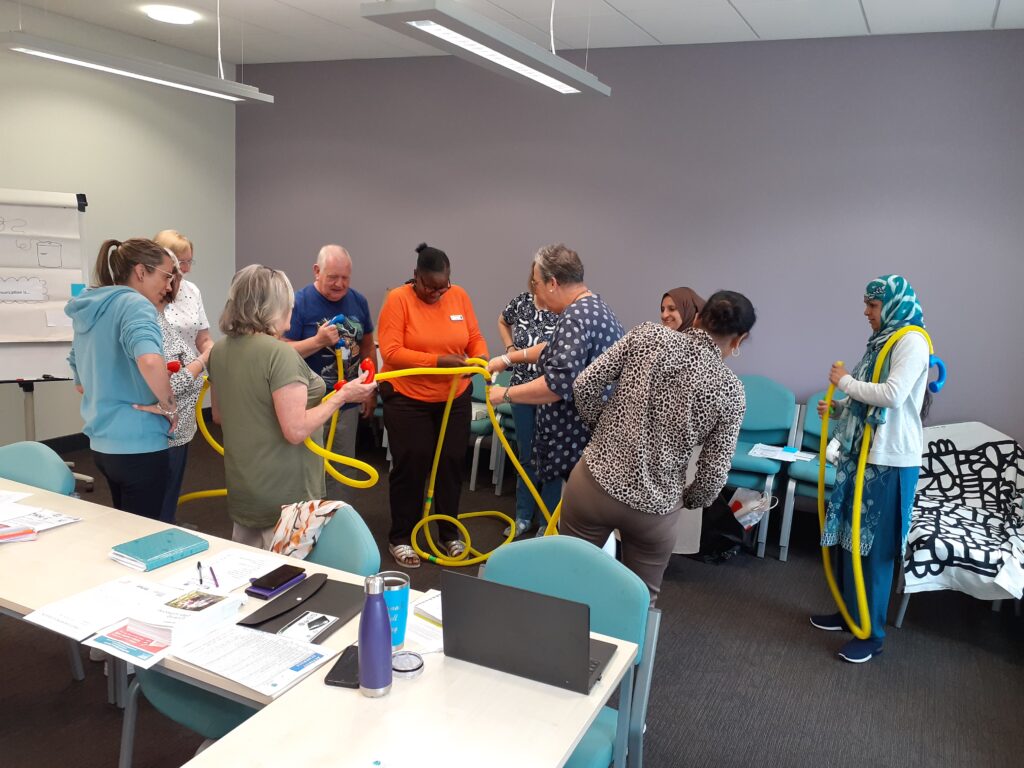 group of people standing in a meeting room, putting together yellow plastic tubing together