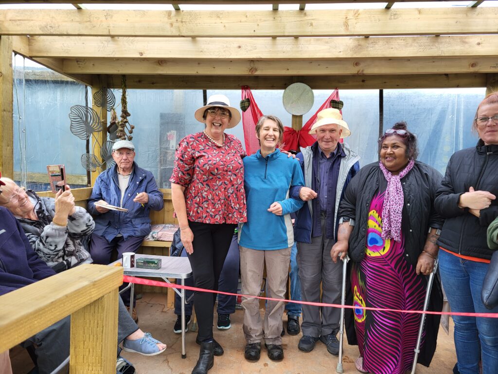 Four people standing smiling to camera, in a new allotment shelter