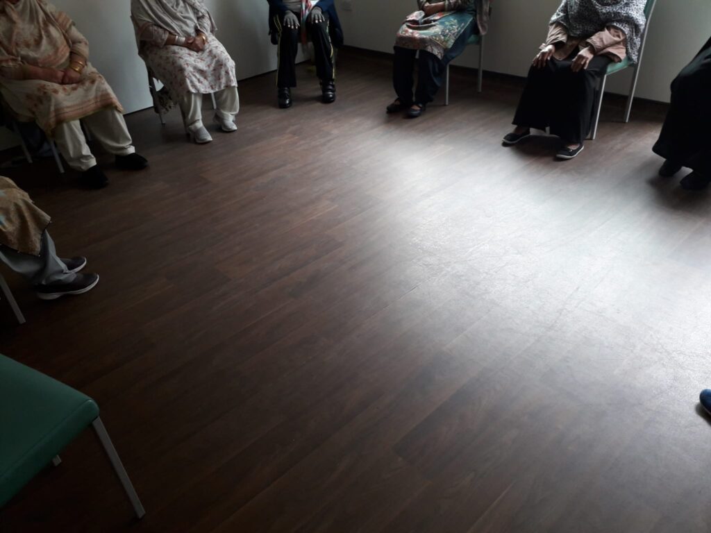 people seated around the edge of a room, facing inwards - shown from the neck down.