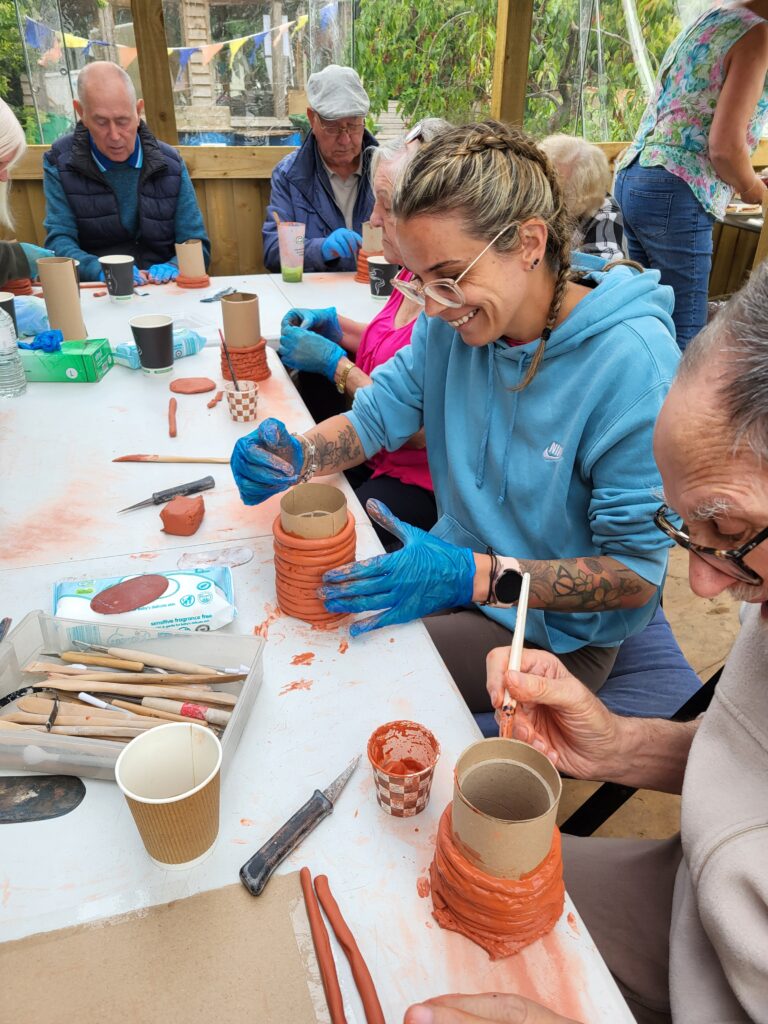 people sitting around a table in a community allotment shelter making clay models together