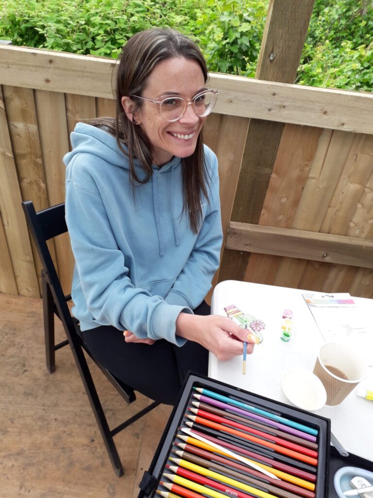 woman sitting at a table with art materials, smiling to camera