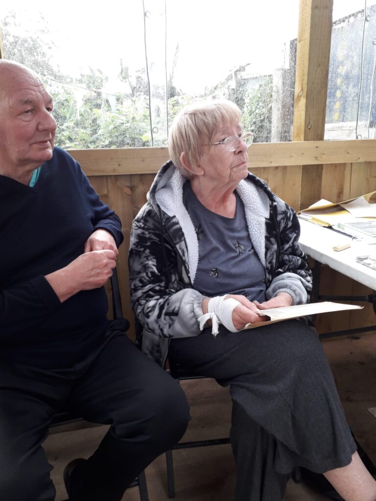 2 people looking up from a piece of paper, sitting in a community allotment shelter