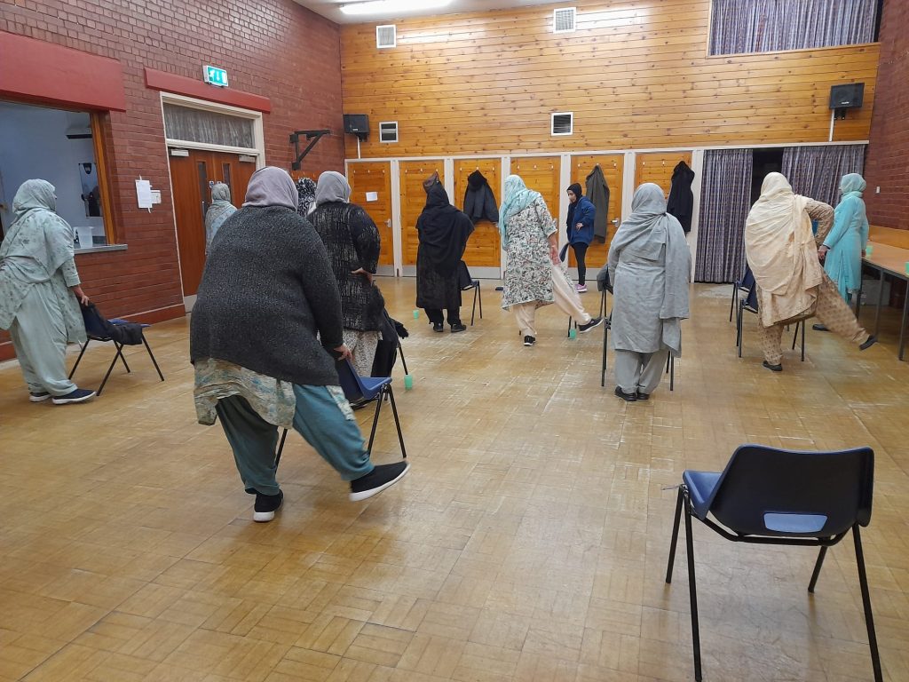 Women standing behind chairs, exercising their legs