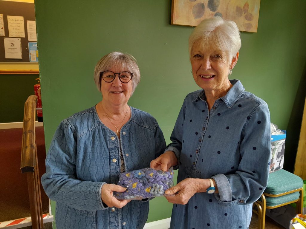 2 women holding a bag of knitted blue flowers