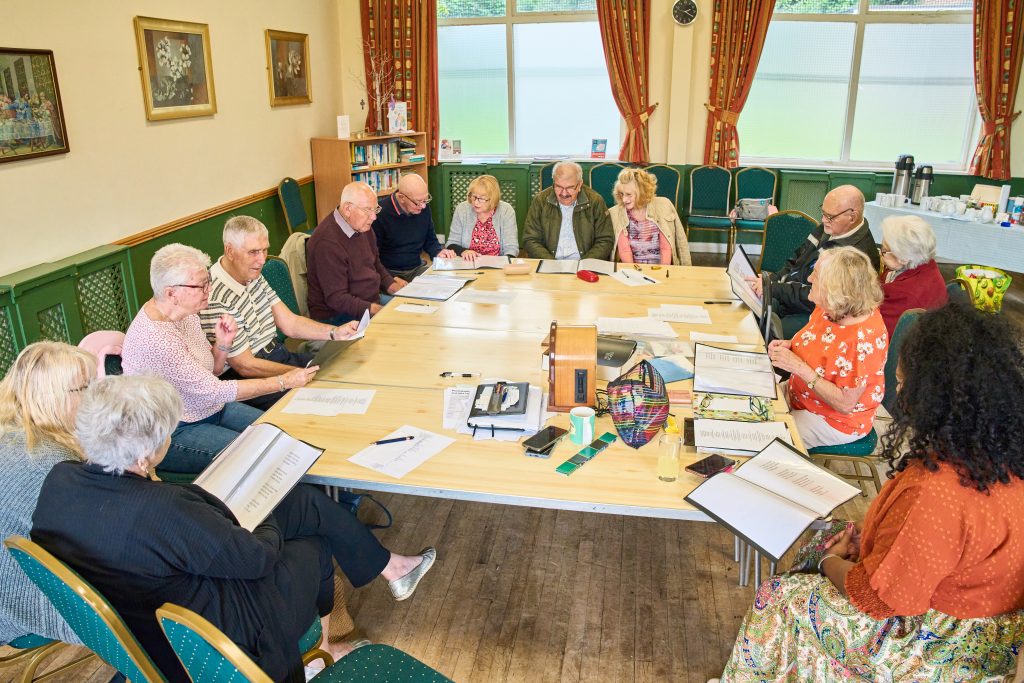 group of people seated around a large table, reading from pieces of paper