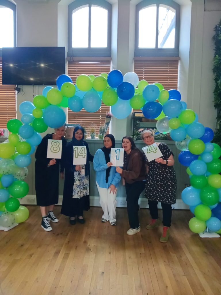 women standing holding large numbers under a balloon arch